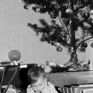Child playing with toy airplane near decorated Christmas tree.
