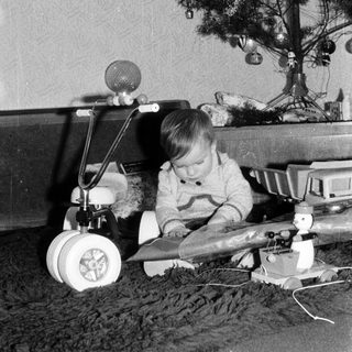 Child playing with toy airplane near decorated Christmas tree.