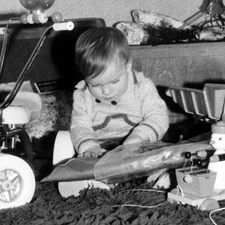 Child playing with toy airplane near decorated Christmas tree.