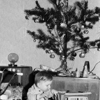 Young child playing with toys near decorated Christmas tree.