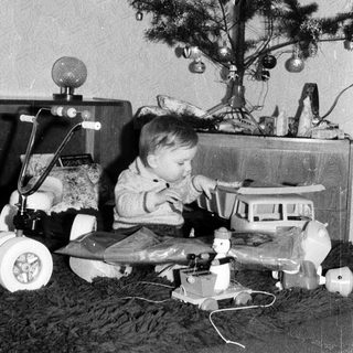 Young child playing with toys near decorated Christmas tree.