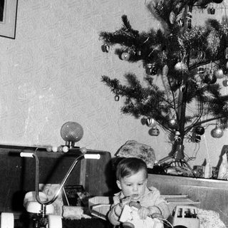 Baby playing with toy near decorated Christmas tree.