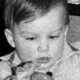 Baby playing with toy near decorated Christmas tree.
