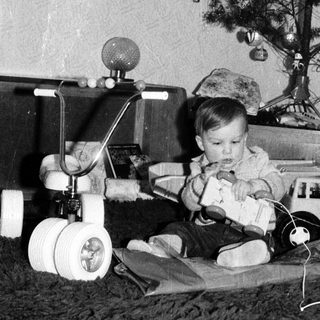 Baby playing with toy near decorated Christmas tree.
