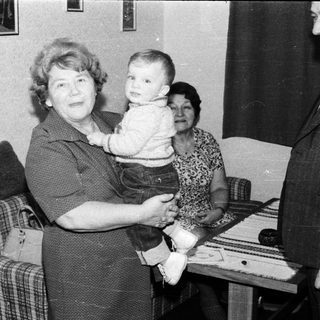 Family portrait with grandmother holding young child indoors.
