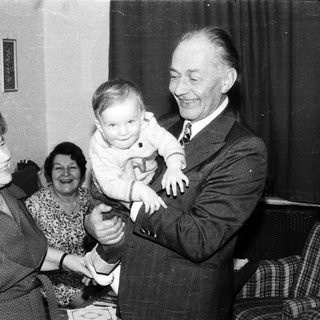 Joyful family moment with elderly couple holding baby indoors.
