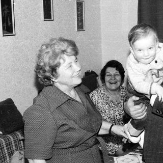 Joyful family moment with elderly couple holding baby indoors.