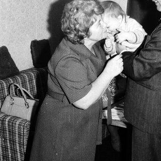 A man kisses a young child on the head while a woman watches.