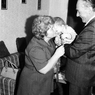 A man kisses a young child on the head while a woman watches.