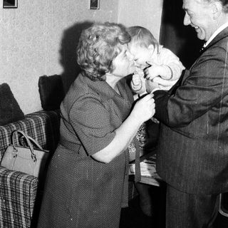 A man kisses a young child on the head while a woman watches.