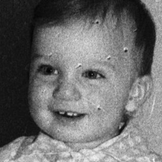 Baby smiling while sitting on a bed.