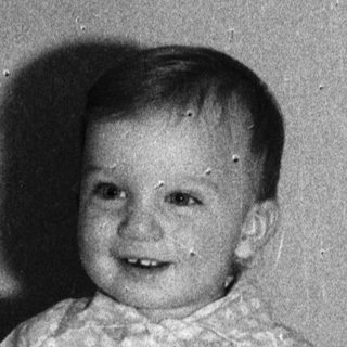 Baby smiling while sitting on a bed.