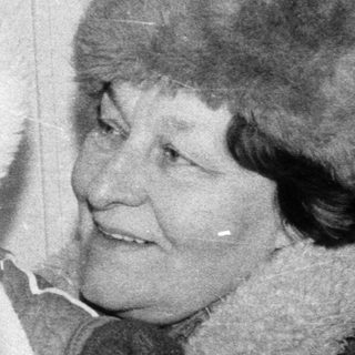 A woman holds a bundled baby indoors.