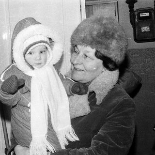 A woman holds a bundled baby indoors.