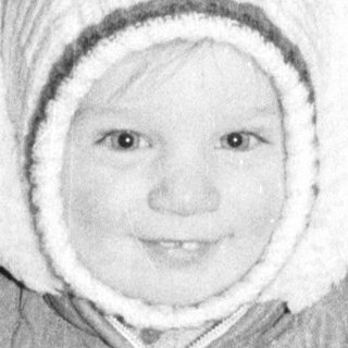 Baby wearing winter snowsuit and hat indoors.