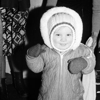 Baby wearing winter snowsuit and hat indoors.