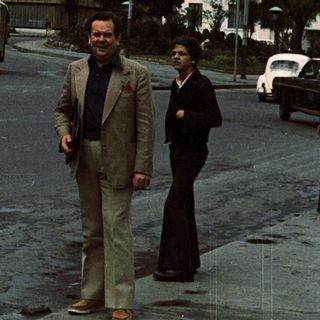 Two men walking near "Palacio del Estado" building.