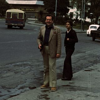 Two men walking near "Palacio del Estado" building.