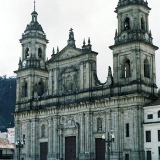 Baroque cathedral with twin towers, urban plaza, people gathered.