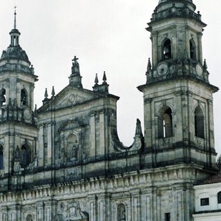 Baroque cathedral with twin towers, urban plaza, people gathered.