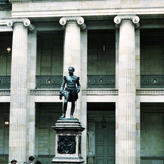 Statue in front of neoclassical building with guards.