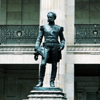Statue in front of neoclassical building with guards.