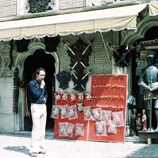 Man standing outside traditional craft shop displaying swords and souvenirs.