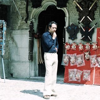 Man standing outside traditional craft shop displaying swords and souvenirs.