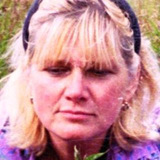 Woman kneeling among purple wildflowers in grassy field.