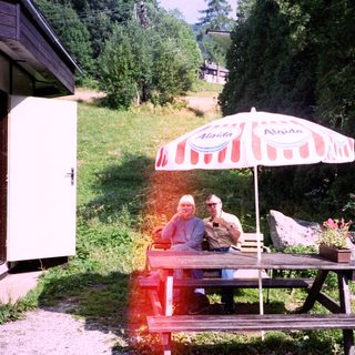 Two people relaxing under umbrella at outdoor picnic table.