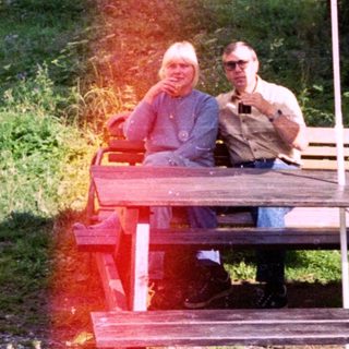 Two people relaxing under umbrella at outdoor picnic table.