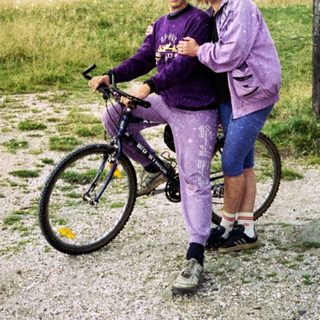 Two people posing with a bicycle in a rural outdoor setting.