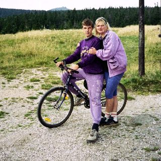 Two people posing with a bicycle in a rural outdoor setting.