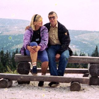 Couple sitting on picnic benches in mountainous outdoor area.