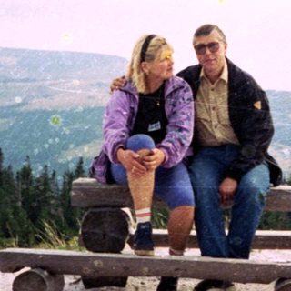 Couple sitting on picnic benches in mountainous outdoor area.