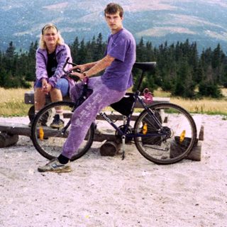 Two people sitting on bikes in mountainous outdoor area.