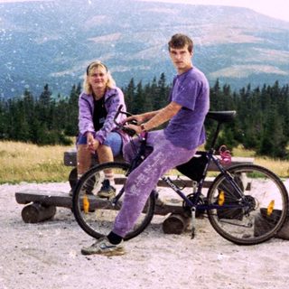 Two people sitting on bikes in mountainous outdoor area.