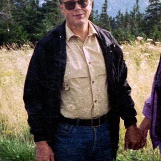 Two people standing outdoors in a scenic, forested hilly area.