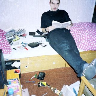 Young man reading in cluttered, disorganized bedroom.