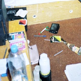 Young man reading in cluttered, disorganized bedroom.