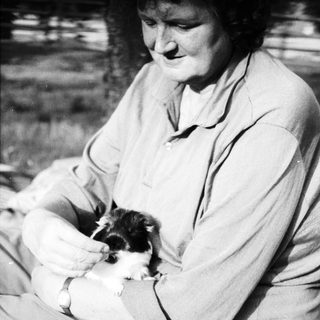 Woman holding small black-and-white puppy outdoors.
