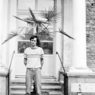 Young man standing outside near potted palm plants.