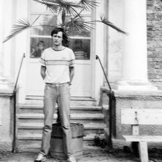 Young man standing outside near potted palm plants.
