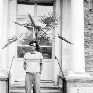Young man standing outside near potted palm plants.