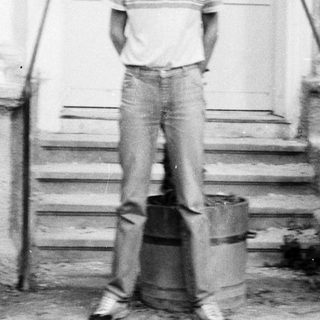 Young man standing outside near potted palm plants.
