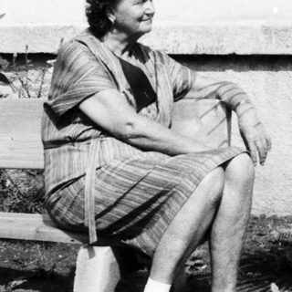 Woman sitting on bench outdoors near potted palm.