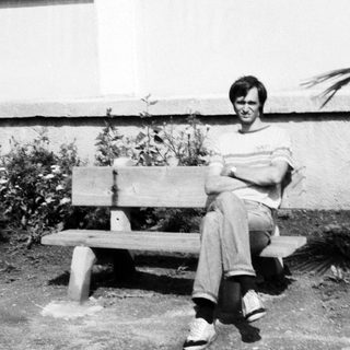 Person sitting on bench outdoors near potted plant.