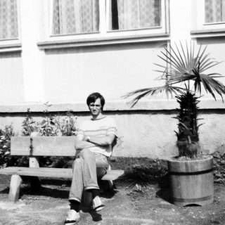 Person sitting on bench outdoors near potted plant.
