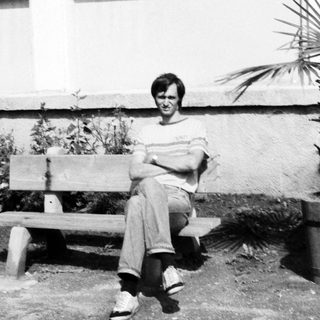 Person sitting on bench outdoors near potted plant.