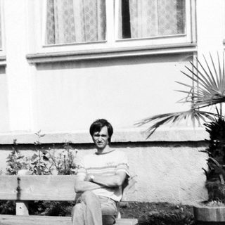 Person sitting on bench outdoors near potted plant.